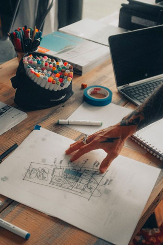 Colaborar-MX-Creacion-Ideas Fotografía de un escritorio con una mano sobre un boceto de una idea de emprendimiento